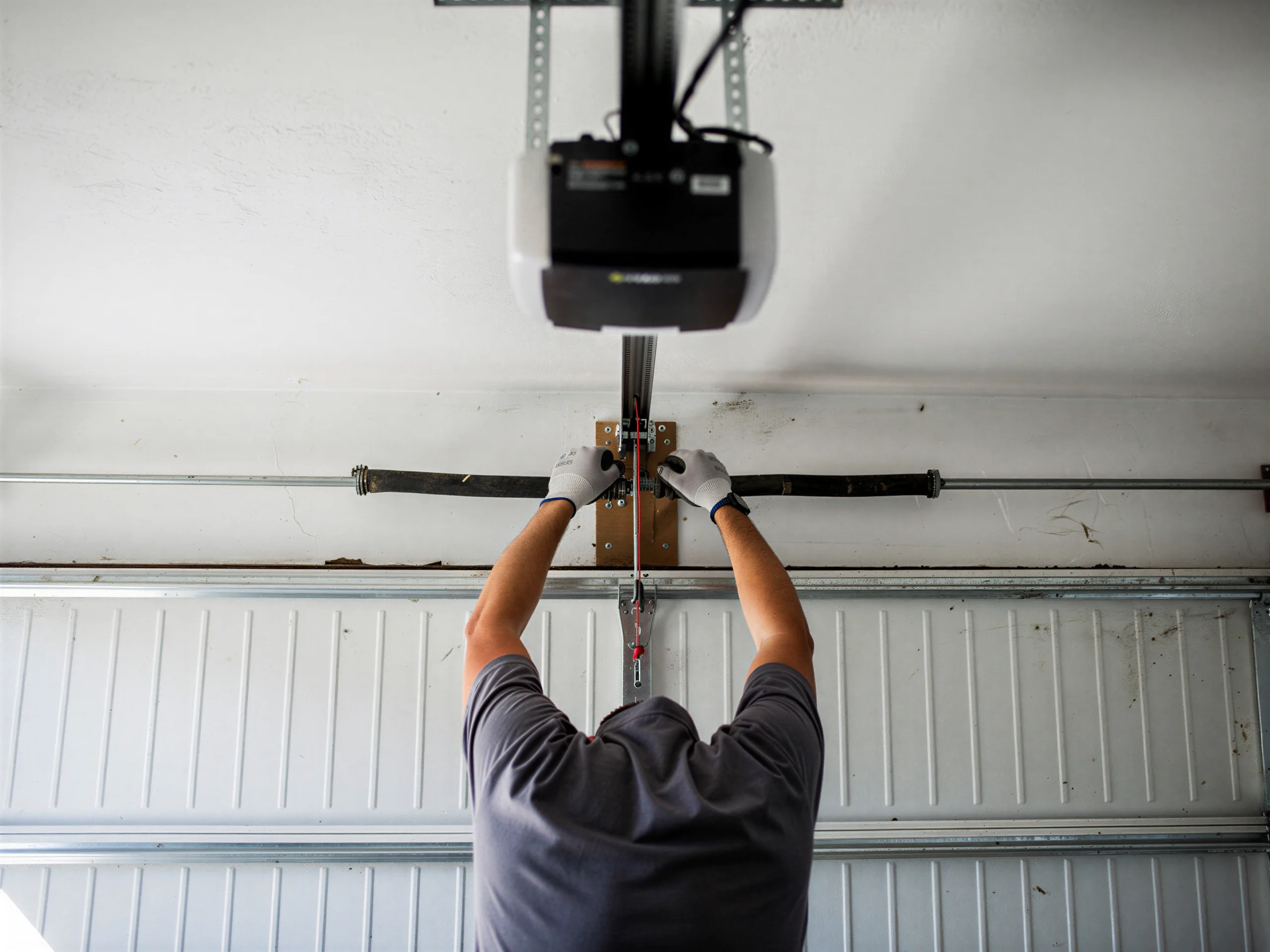 A technician adjusts a torsion spring above a white garage door.